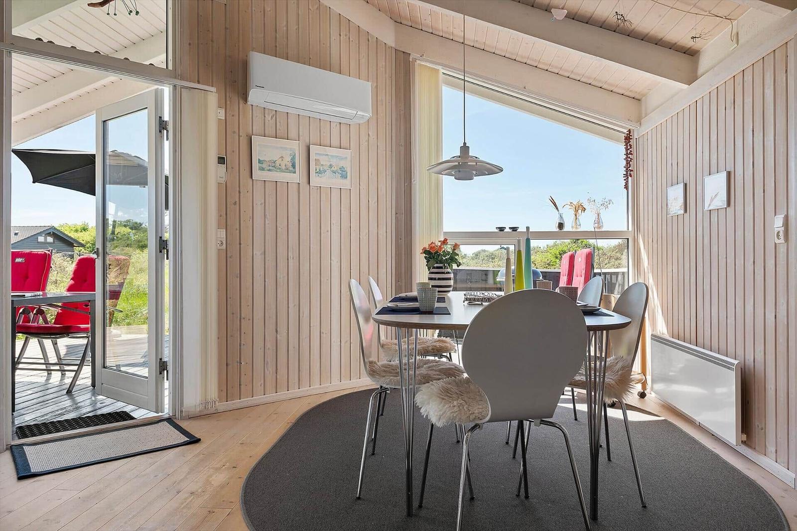 Essbereich mit Tisch, Stühlen und Blick auf Balkon. Holzwände und große Fenster.