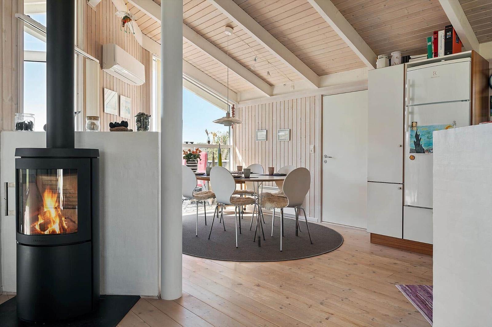 Wohnraum mit Kamin, Esstisch und Küchenbereich unter Holzdecke.