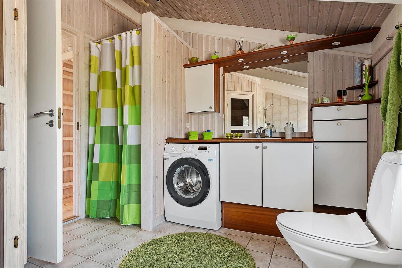 Badezimmer mit Waschmaschine, Spiegelschrank und grünem Duschvorhang.