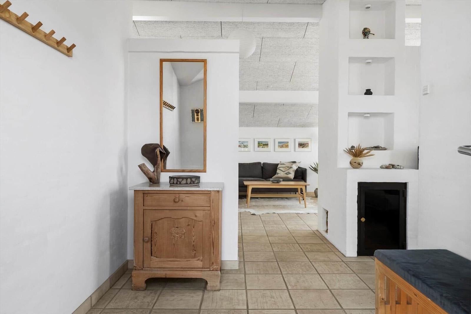 Eingangsbereich mit Holzschrank, Spiegel und Blick in Wohnzimmer mit Sofa und Kamin.