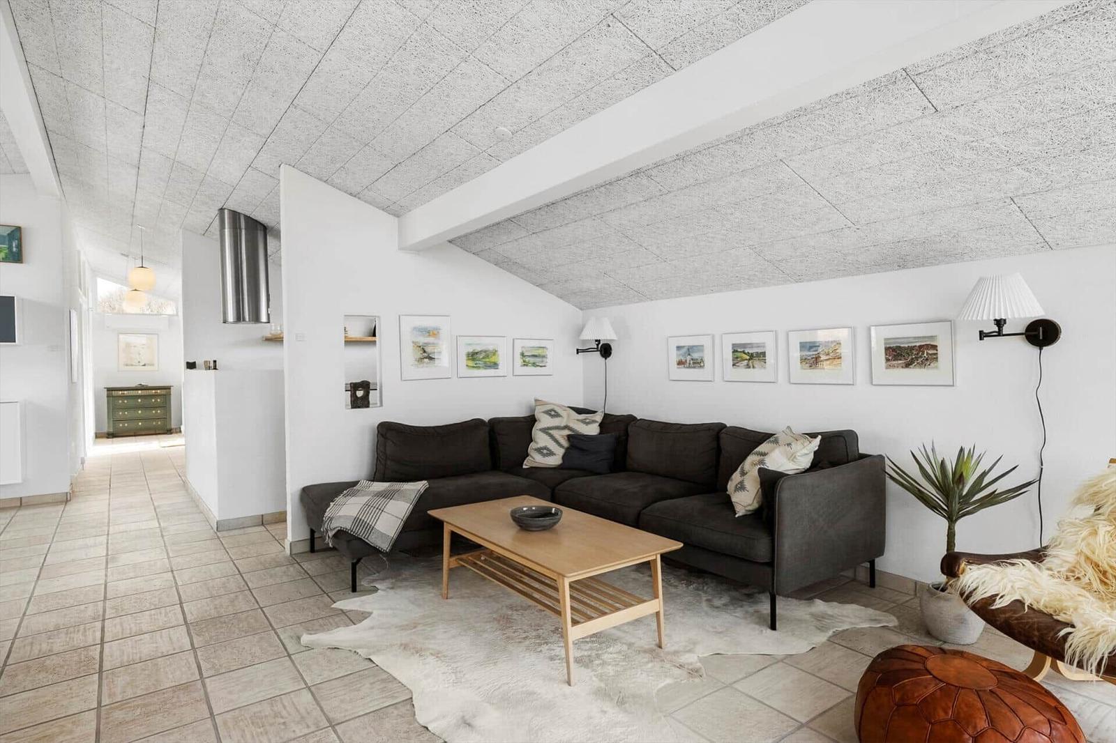 Wohnzimmer mit grauem Sofa, Holztisch und Tierfellteppich unter schrägem Deckenverlauf.