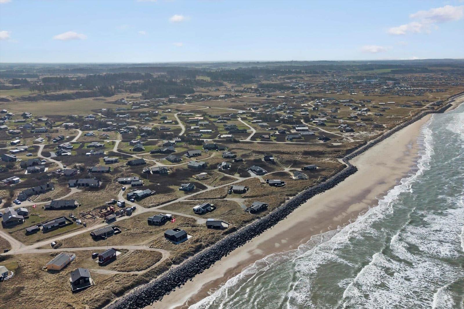 Aerial view of coastal village with houses, paths, and sandy beach alongside waves.