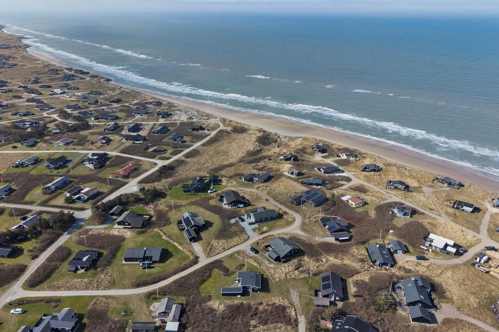 Luftbild von Strandhäusern mit Dünen und Meer im Hintergrund.