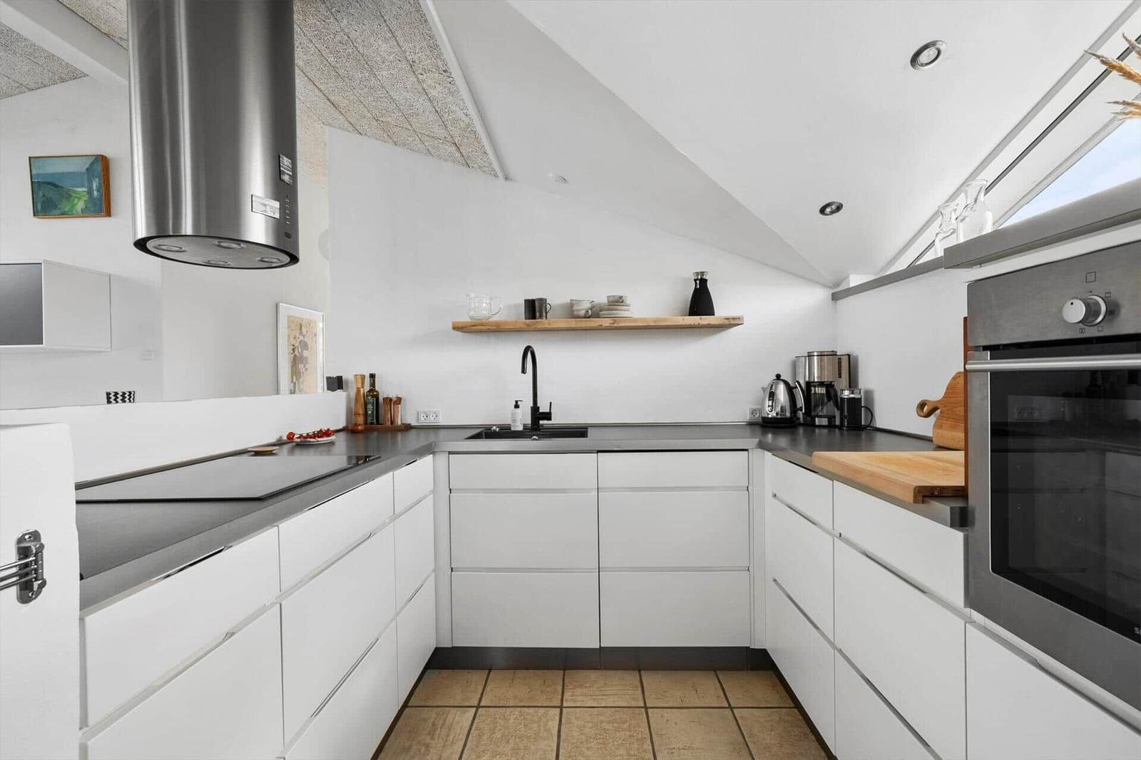 Moderne Küche mit weißen Schränken, Edelstahlgeräten und Holzregal.