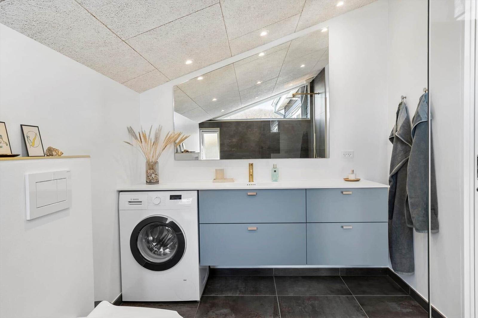 Badezimmer mit Waschmaschine, Spiegelschrank und dunklen Fliesen.