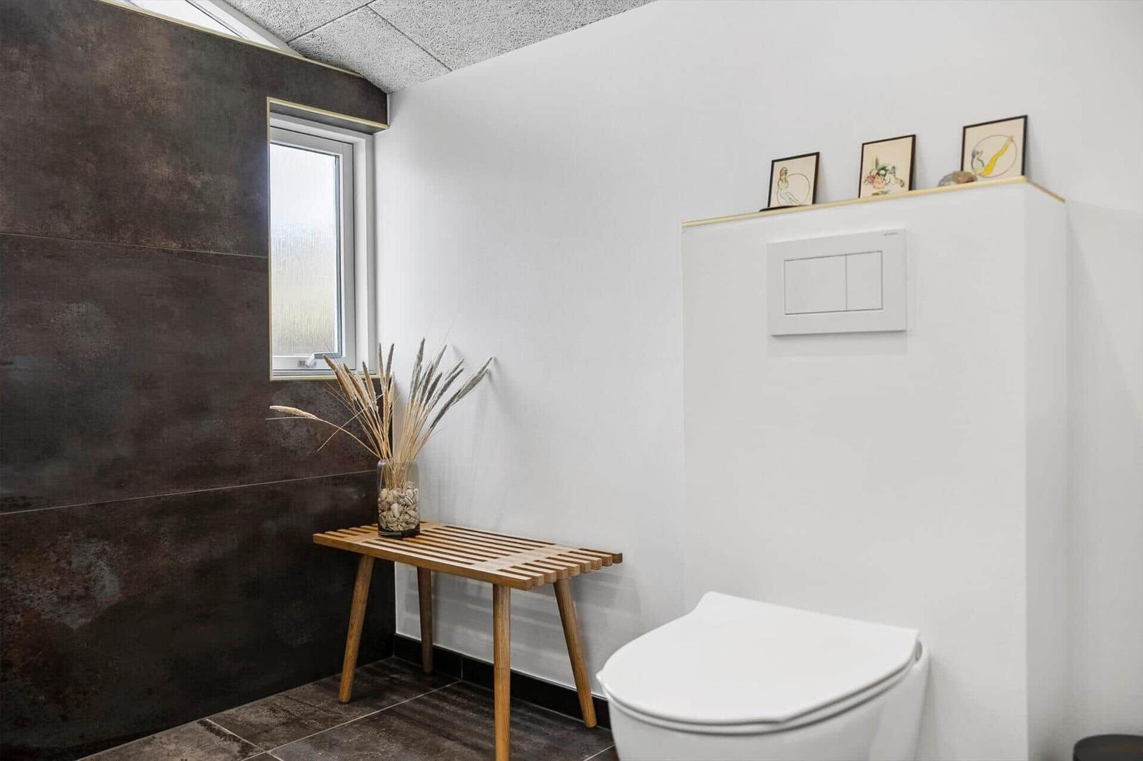 Badezimmer mit Toilette, Holztisch und Fenster. Wand aus dunklem Stein.