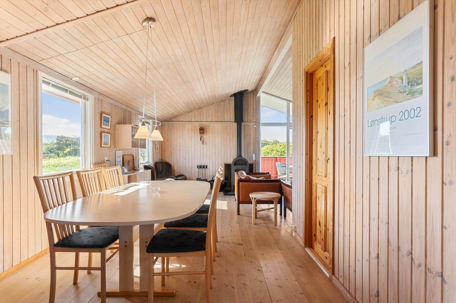 Essbereich mit Tisch und Stühlen, Holzwand und -boden, Kamin und Fenster.