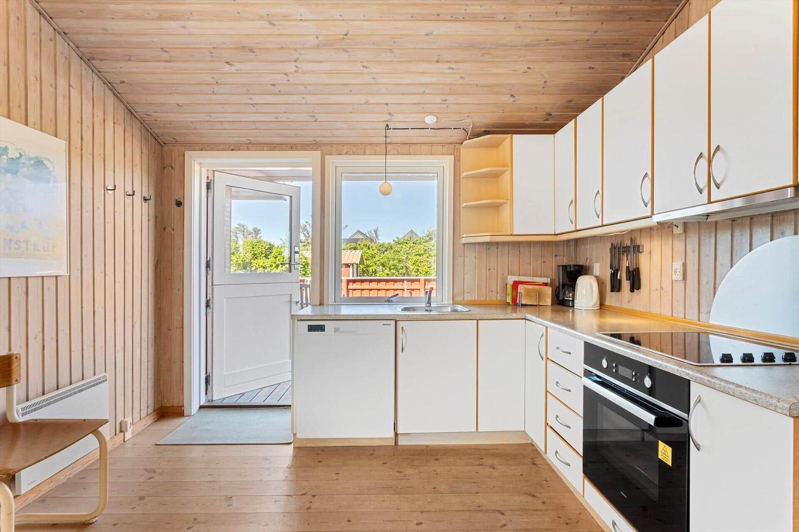 Küche mit weißen Schränken, Holzwand und Fenster zum Balkon.