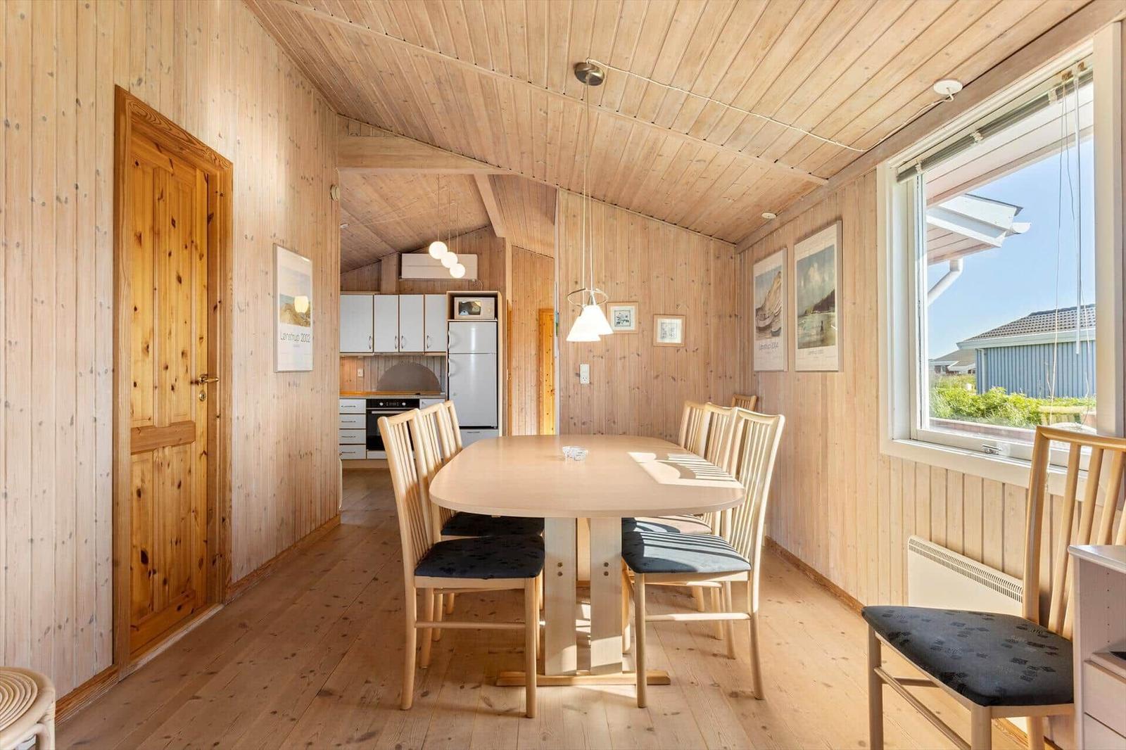 Essbereich mit Holztisch und Stühlen, Küchenbereich im Hintergrund, Holzwände und -boden.