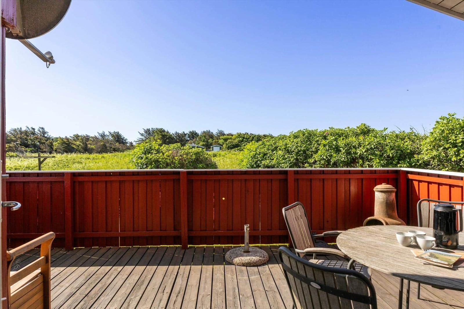 Terrasse mit Tisch, Stühlen und Grill. Blick auf grüne Landschaft und Himmel.