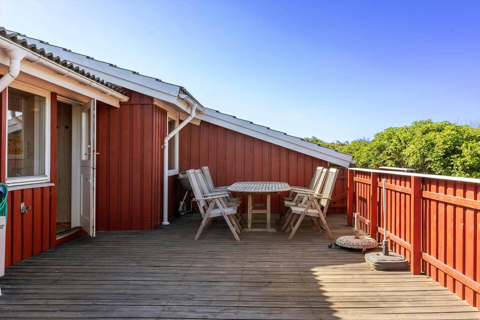 Terrasse mit Tisch und Stühlen vor einem roten Haus mit Grill.
