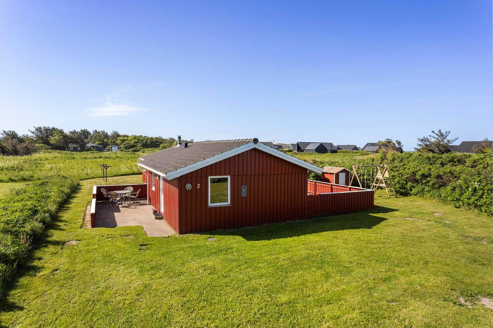 Rotes Ferienhaus mit Terrasse und Garten. Hinterhof mit Schaukel und kleinem Holzhaus.