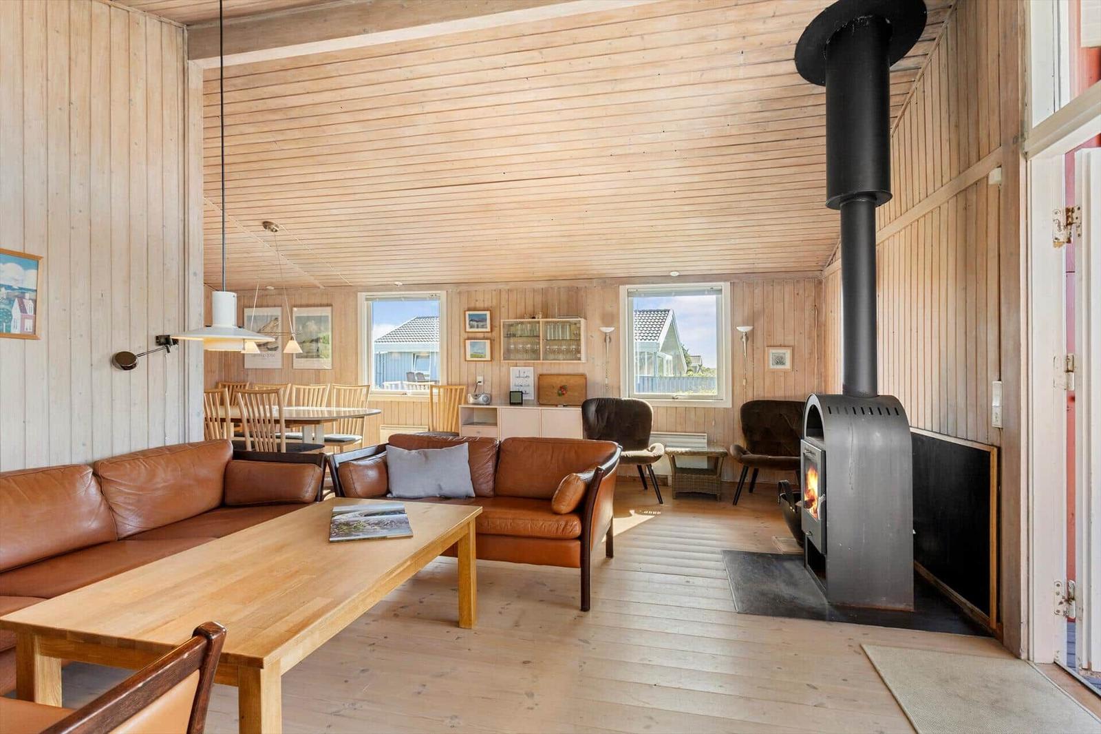 Wohnraum mit Holzwänden, Sofa, Kamin und Fenstern zum Blick nach draußen.