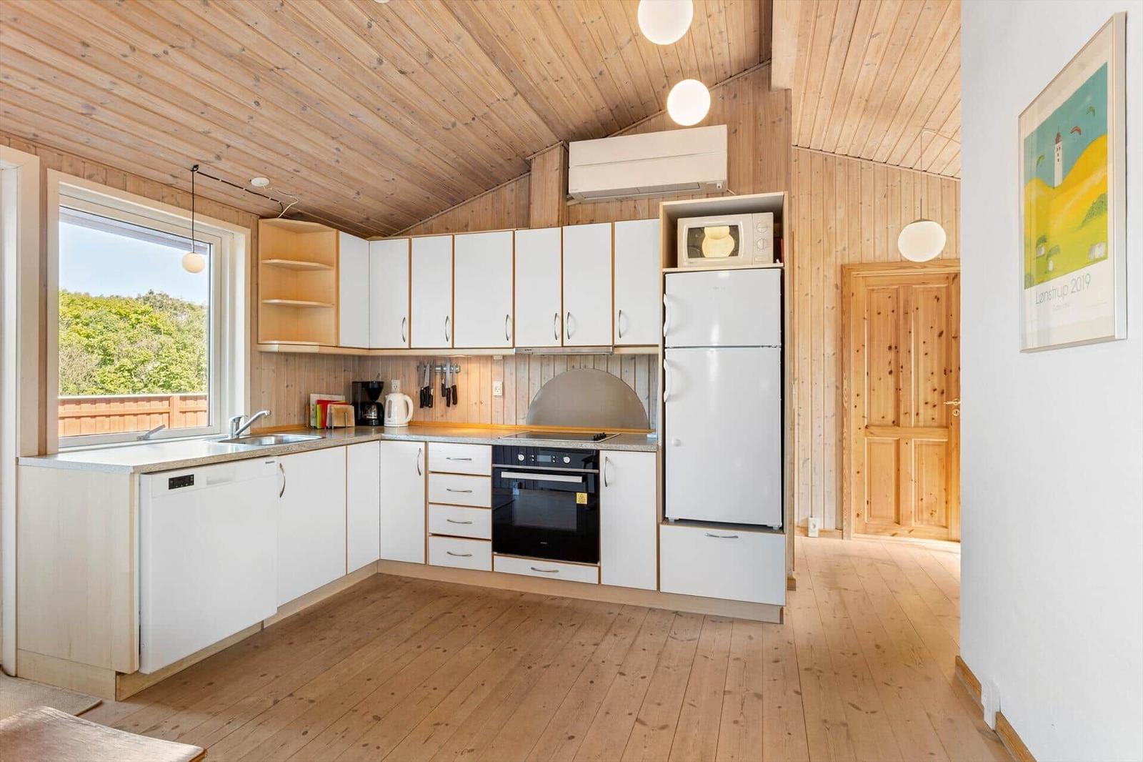 Küche mit weißer Einbauküche, Kühlschrank und Fenster mit Blick nach draußen.