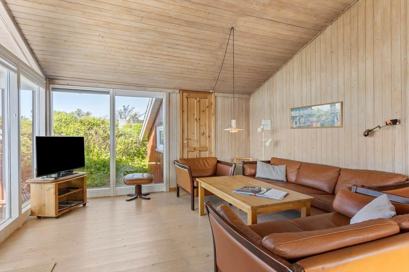 Wohnzimmer mit Holzwand, braunem Ledersofa, TV und Glasfront zur Außenterrasse.