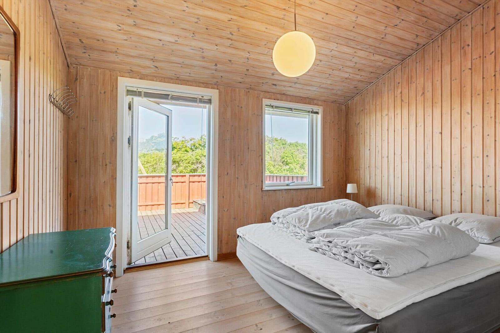 Schlafzimmer mit Holzwand, Bett, Fenster und Tür zur Terrasse.