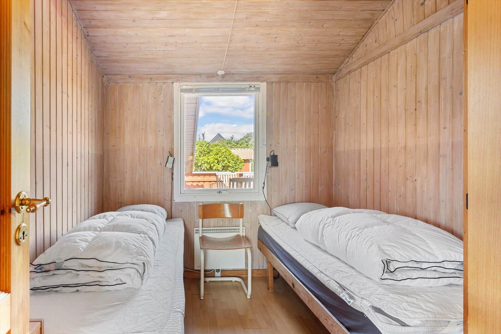Zwei Betten in einem Holzraum mit Fenster und Stuhl.