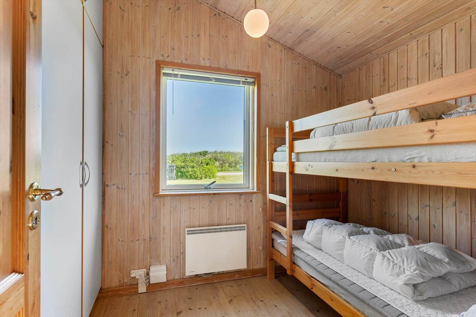 Zimmer mit Holzwand, Doppelstockbett und Fenster mit Blick auf Grünfläche.
