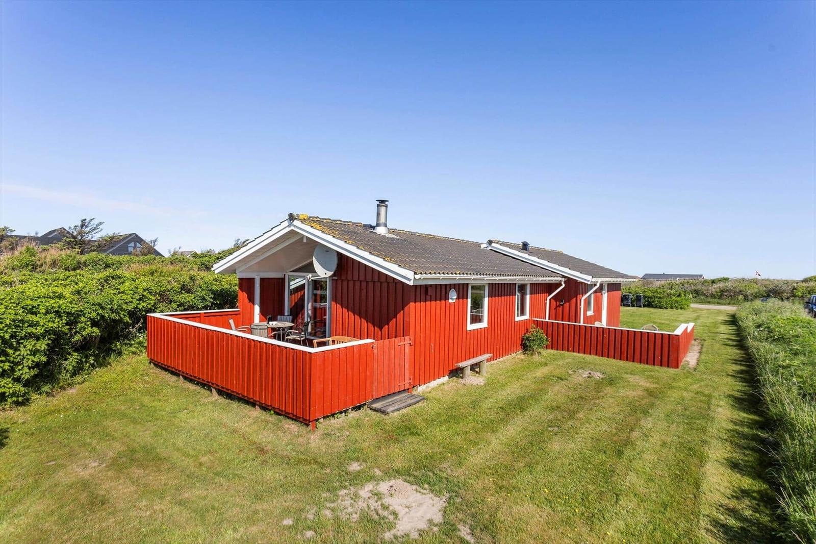 Rotes Holzhaus mit Terrasse und Garten. Klare Sicht auf den Himmel.