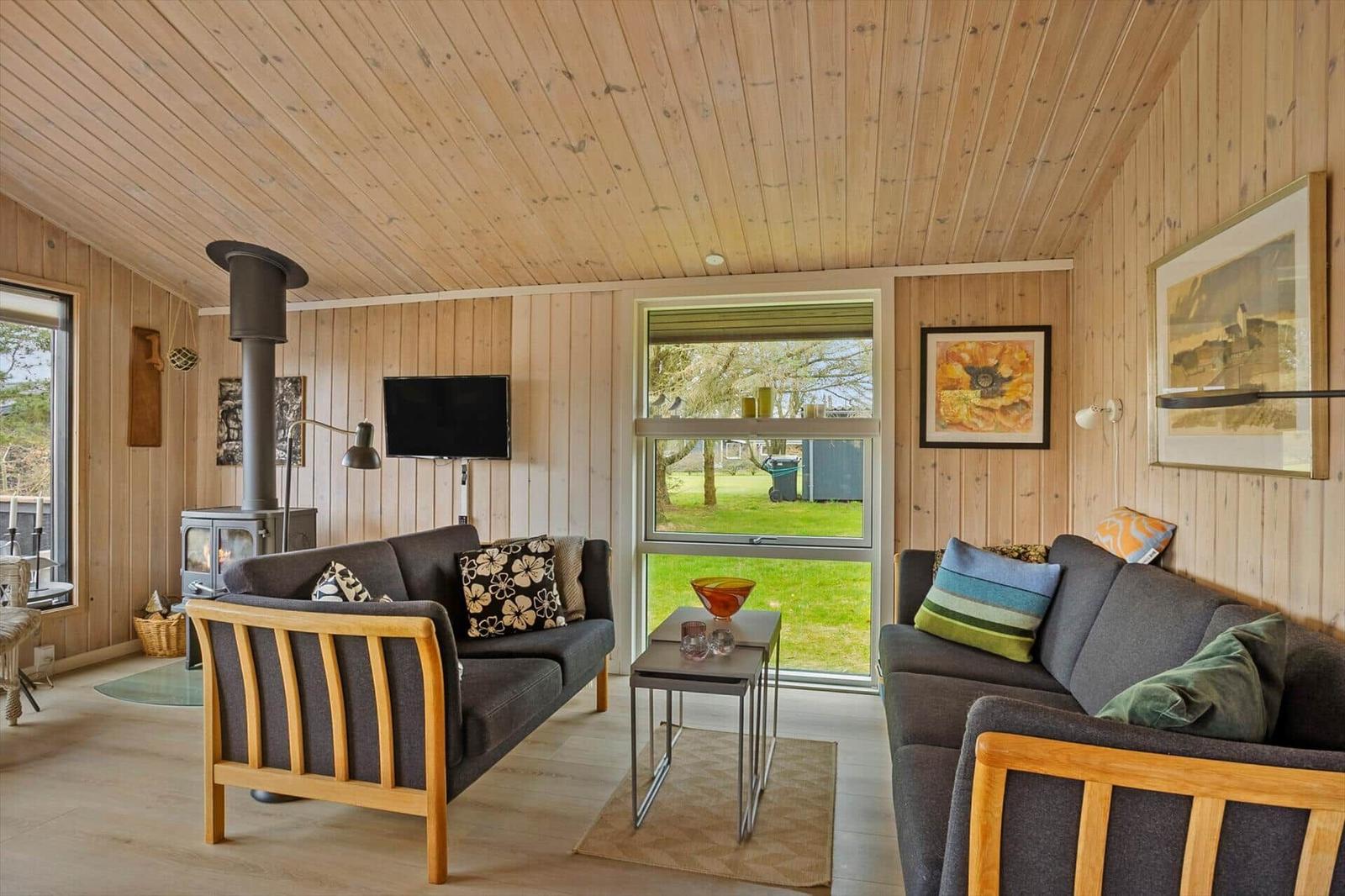 Wohnzimmer mit zwei Sofas, Kamin und großen Fenstern zur grünen Außenansicht.