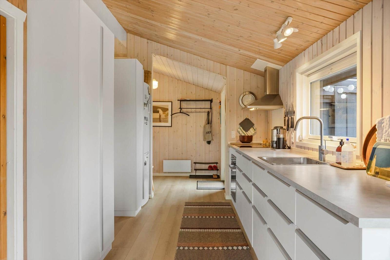 Küche mit weißen Schränken, Holzwand und -boden. Fenster, Spüle und Kochfeld sichtbar.