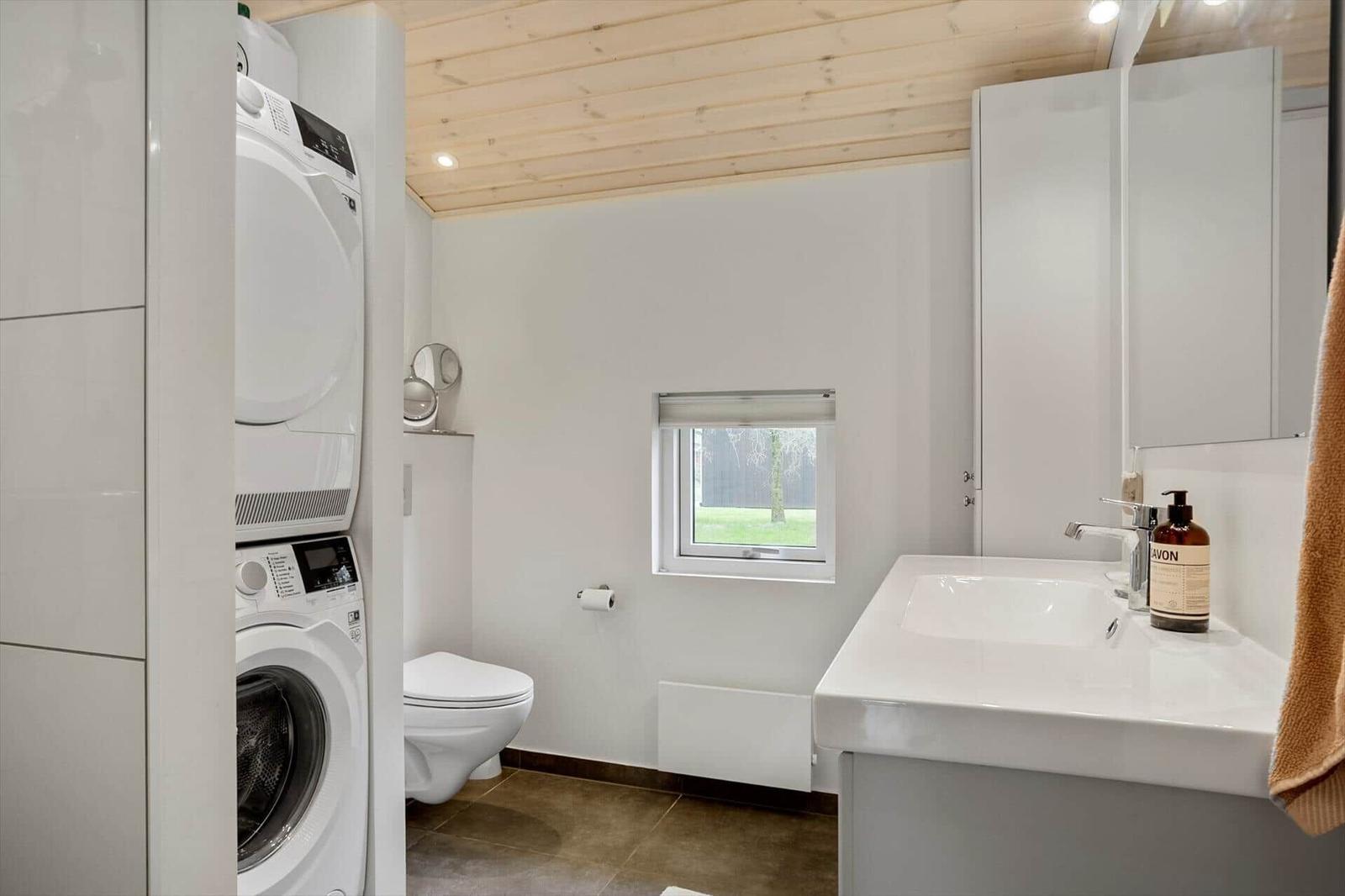 Badezimmer mit Waschmaschine, WC und Waschbecken. Holzdecke und kleines Fenster.
