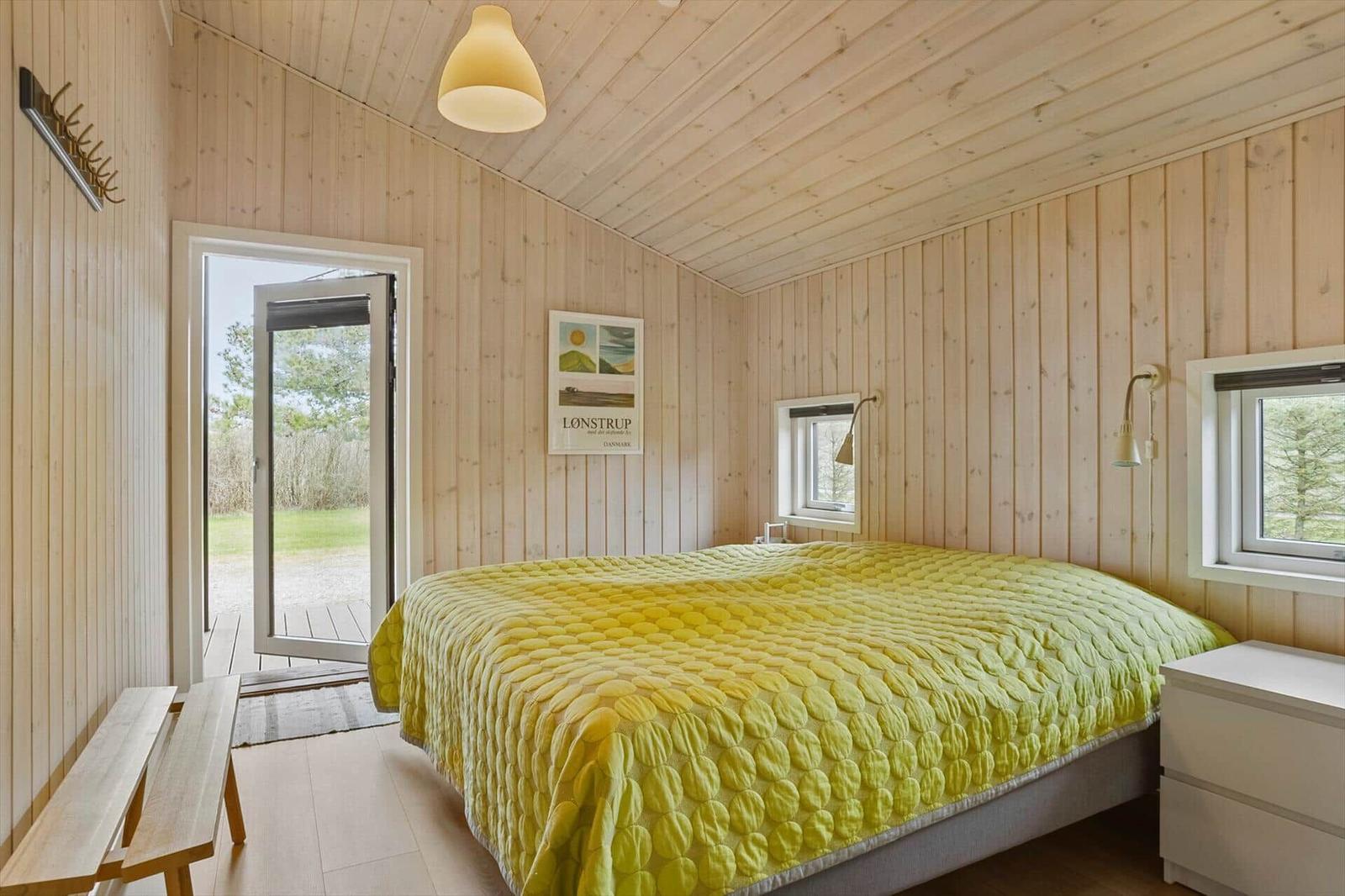 Schlafzimmer mit Holzwand, gelbem Bettbezug und Tür zum Außenbereich.