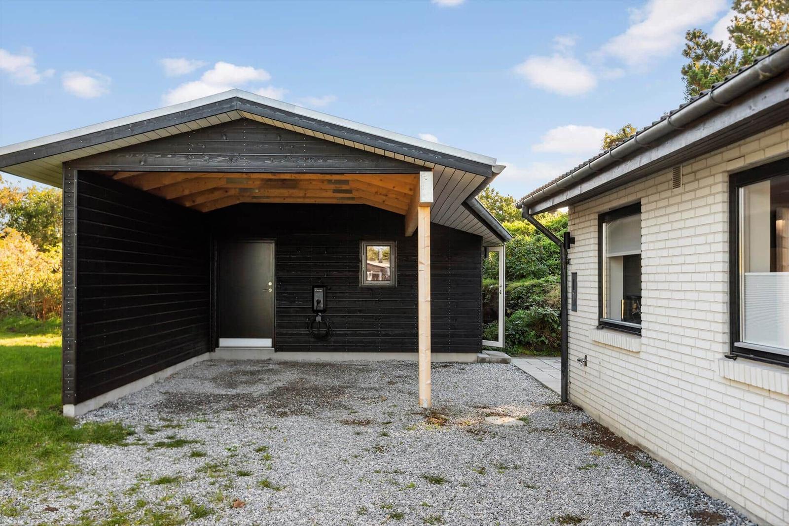 Ein modernes Carport mit schwarzer Holzfassade und einem Kfz-Ladepunkt.