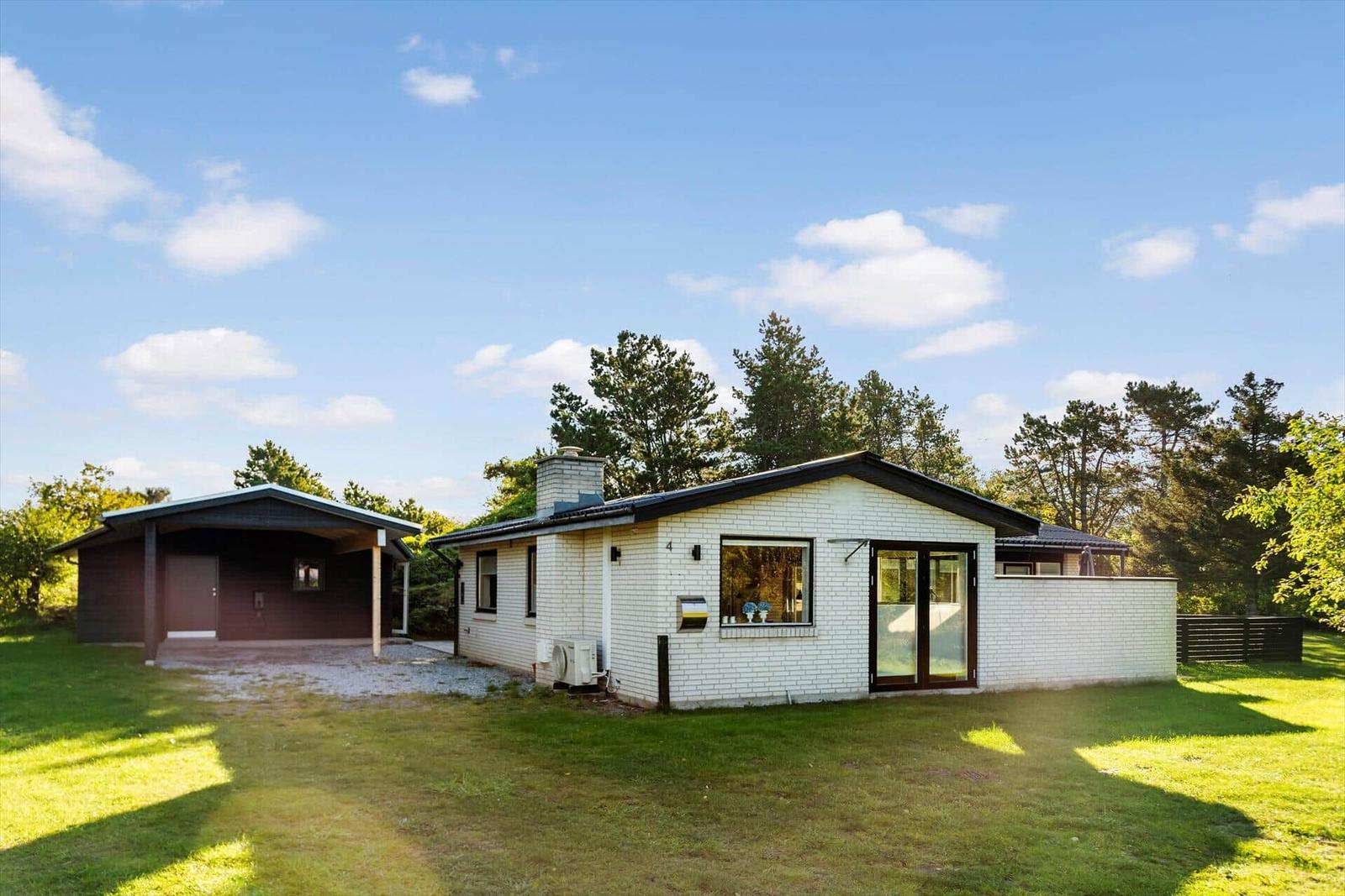 Moderne Villa mit weißen Wänden und dunklem Dach. Grünfläche und Bäume umgeben das Haus.