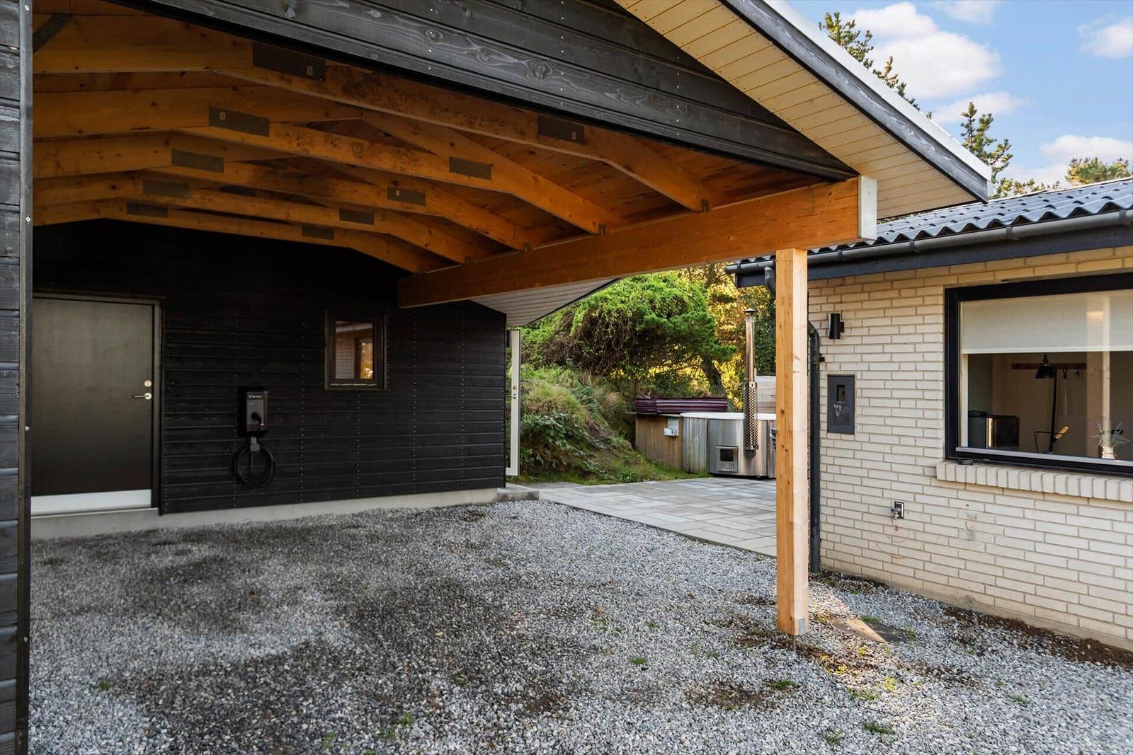 Außenbereich mit Holzüberdachung, grauem Kies und modernem Haus.