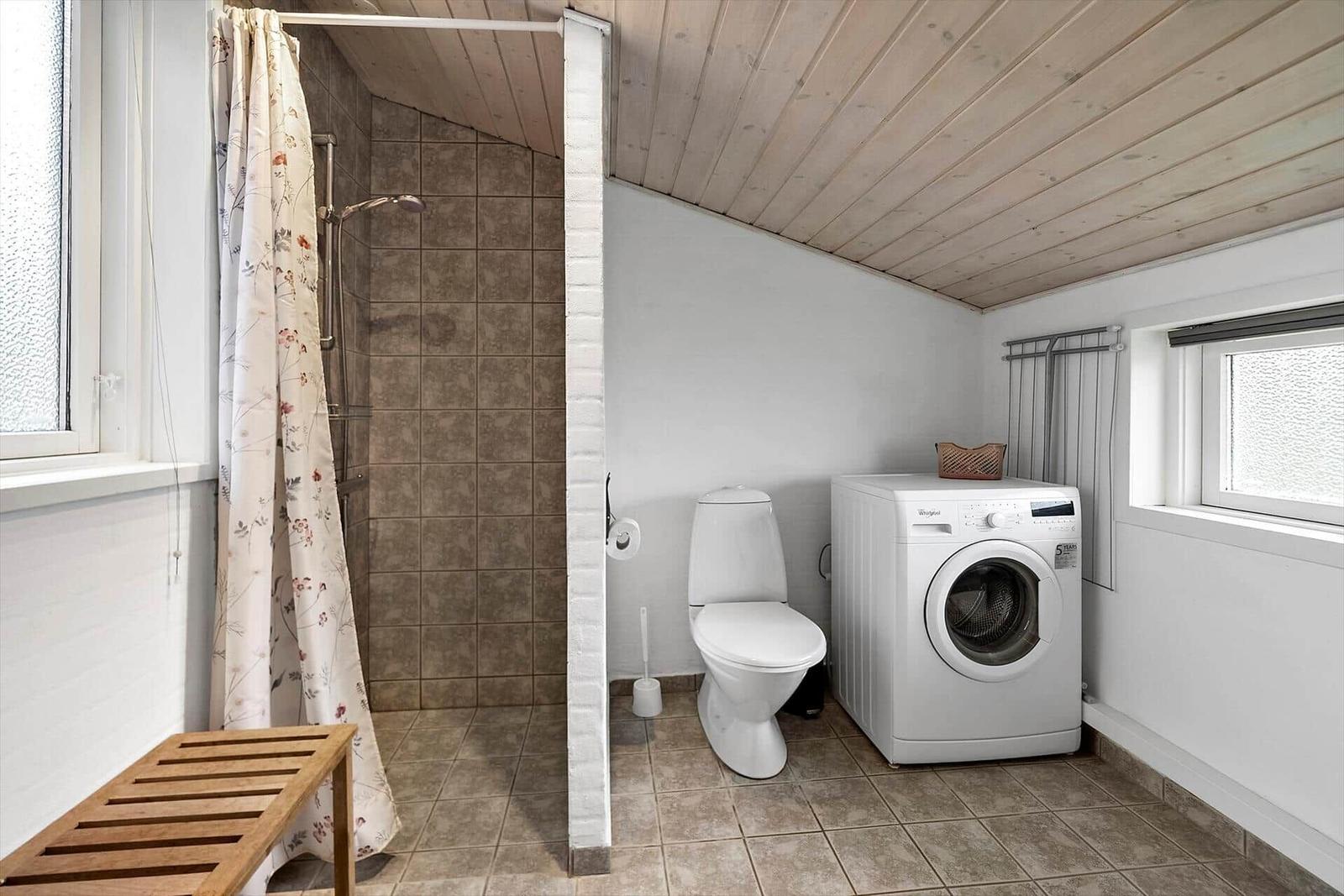 Bad mit Dusche, Toilette und Waschmaschine. Holzdecke und Fenster.