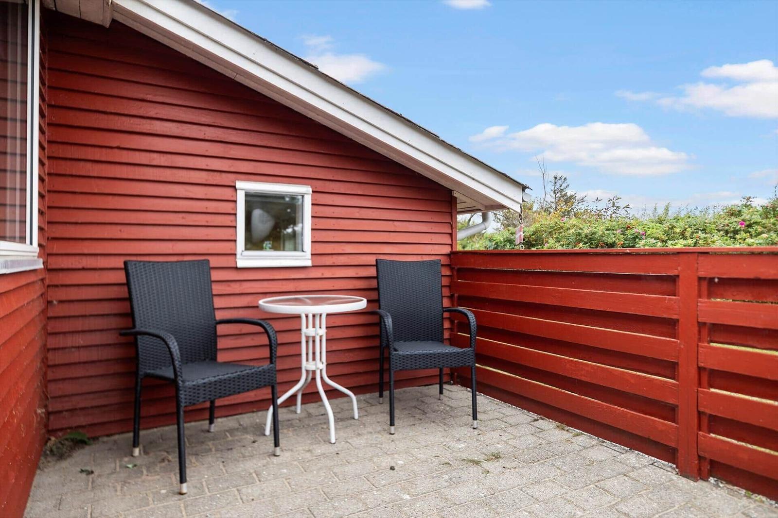 Roter Holzaussenbereich mit Tisch und zwei Stühlen. Hinterhof mit Pflanzen.