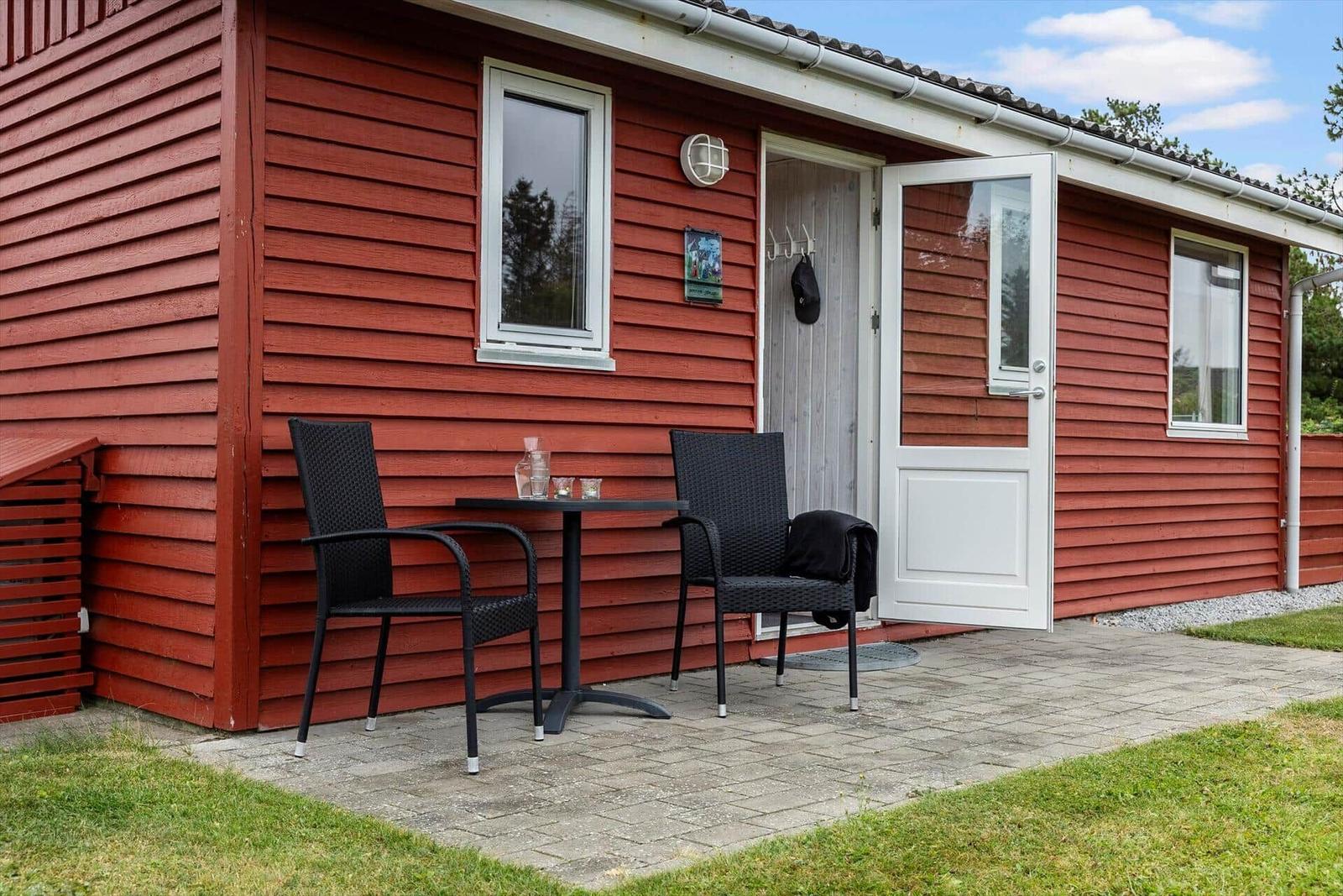 Rotes Holzhaus mit Terrasse, Tisch und zwei Stühlen vor der Tür.