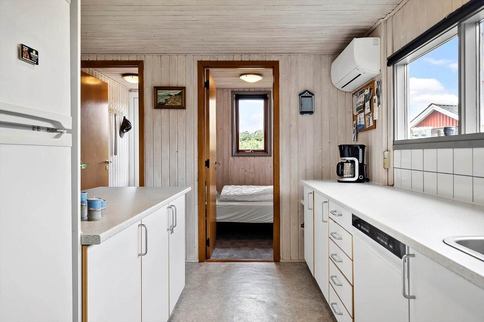 Küche mit Blick in Schlafzimmer und Wohnbereich. Holzwände und weiße Schränke.