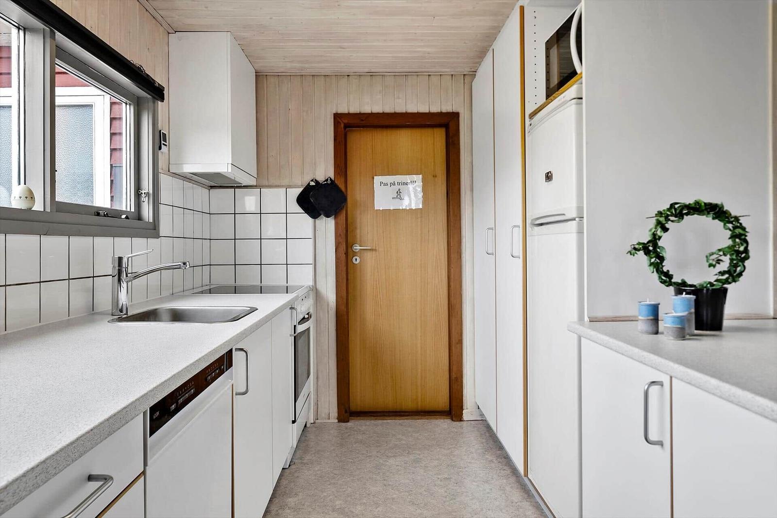 Küche mit Arbeitsplatte, Spüle, Kühlschrank und Tür im Hintergrund.