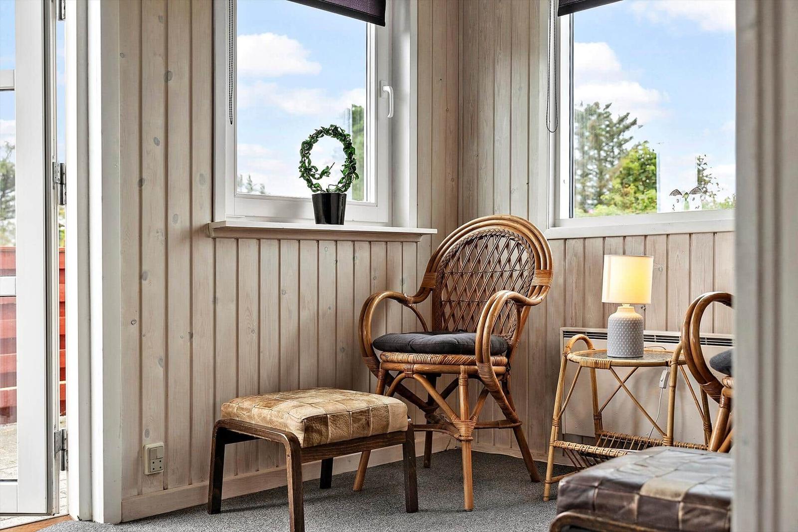 Rattan-Stuhl mit Kissen, Beistelltisch und Pflanze vor Fenster mit Blick auf Grün.