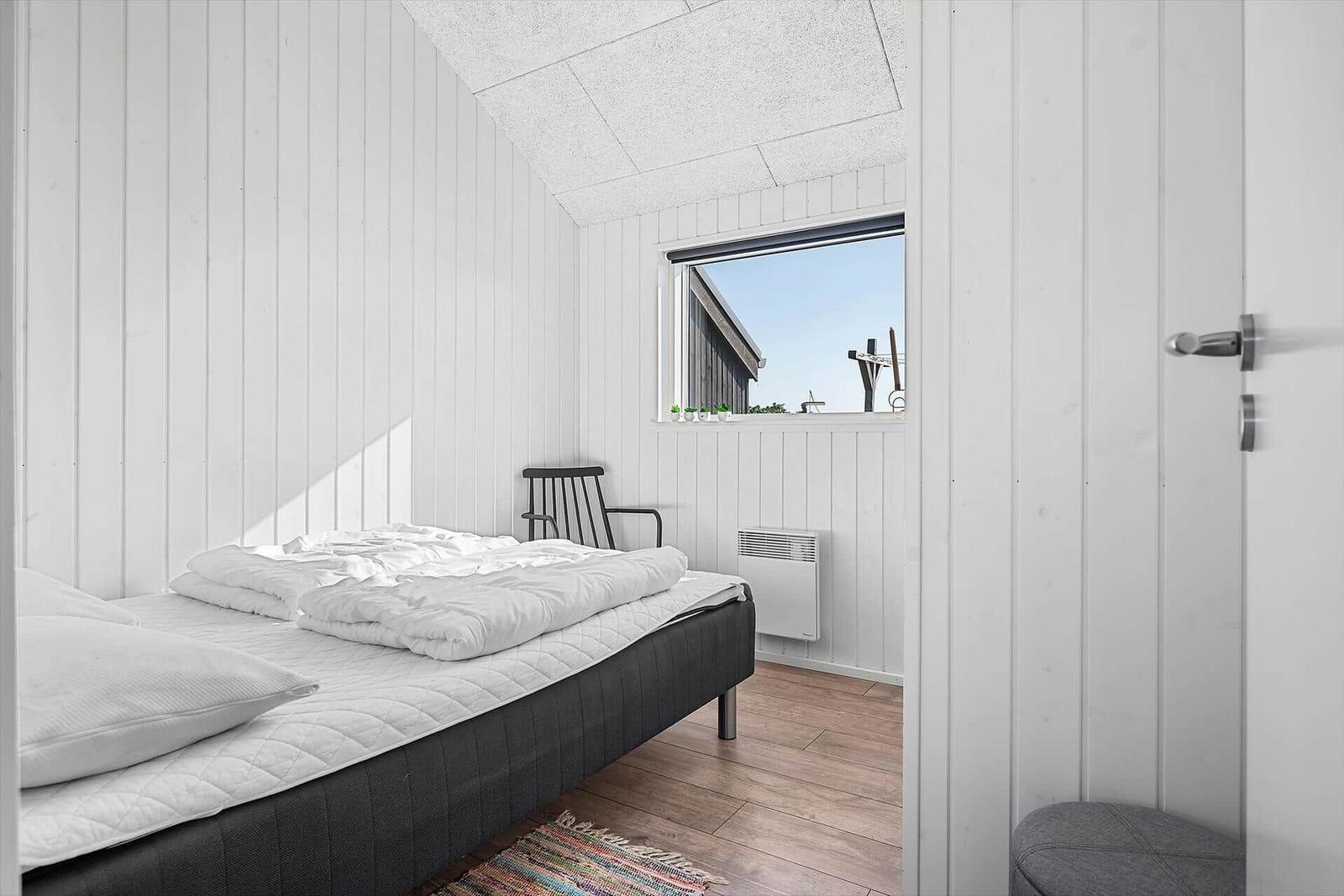 Schlafzimmer mit Bett, Stuhl und Fensterblick auf Gebäude.