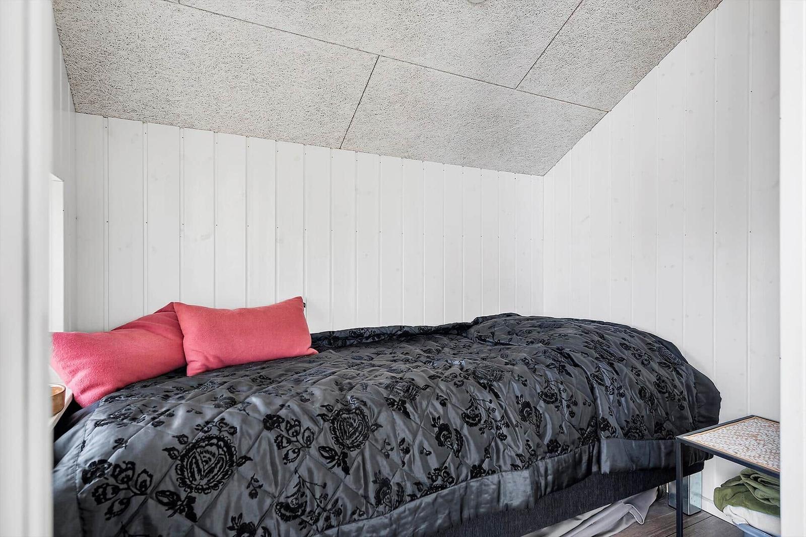 Schlafzimmer mit Bett, rosa Kissen und floraler Bettdecke. Weiße Wände und Decke.