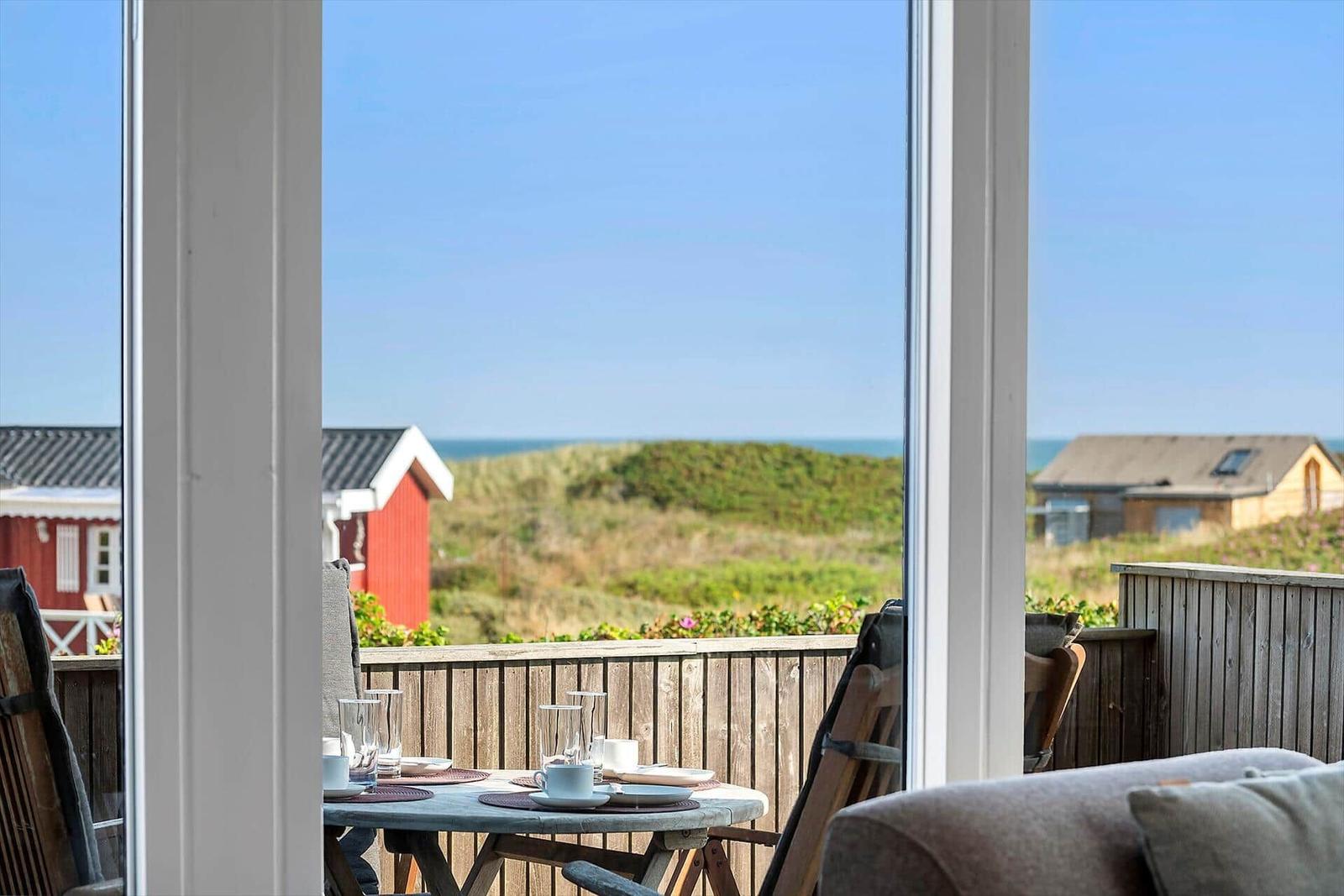 Terrasse mit Tisch und Stühlen bietet Blick auf Strand und Dünen.