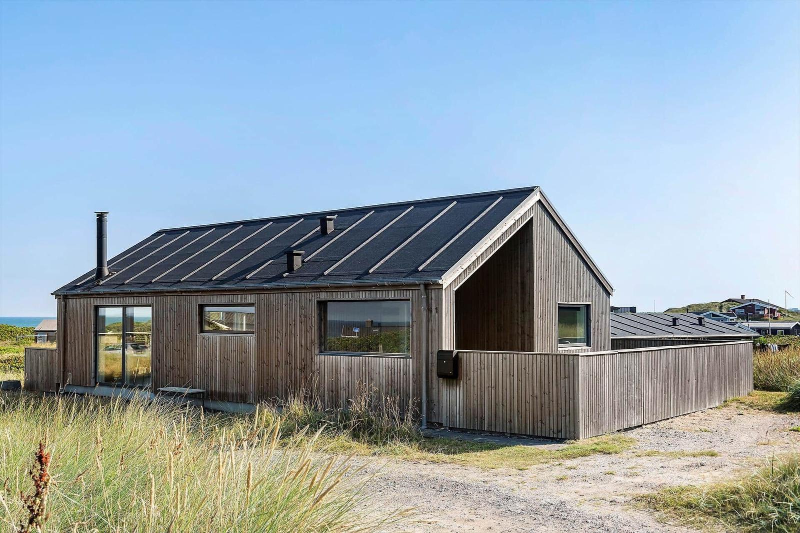 Moderne Holzhütte mit großem Fenster und Dachgaube. Blick aufs Meer.