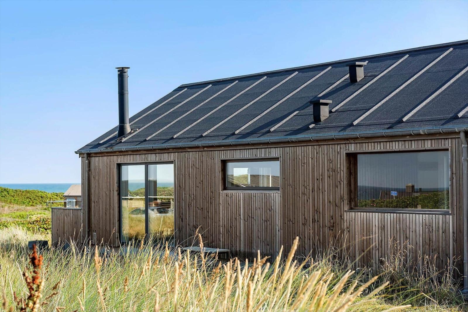 Moderne Holzhütte mit großem Fenster und Dachrohr. Blick auf das Meer.