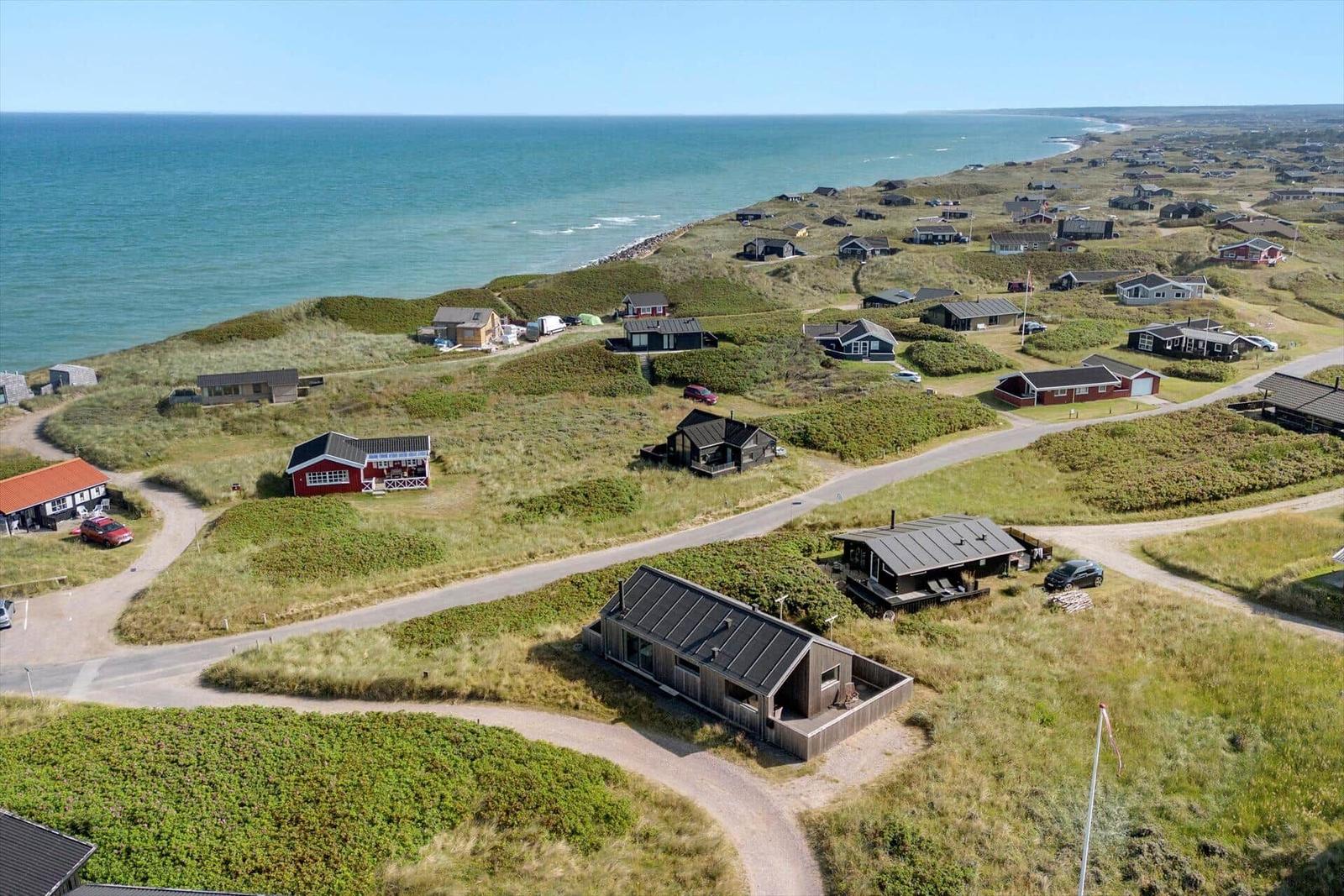 Küstenansicht mit mehreren Häusern auf grünen Dünen und dem Meer im Hintergrund.