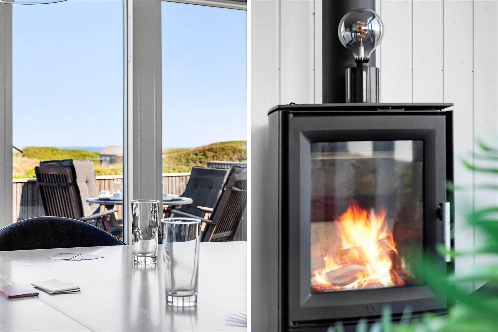 Tisch mit Gläsern und Blick auf Terrasse mit Sitzgelegenheiten. Kamin mit brennendem Feuer.
