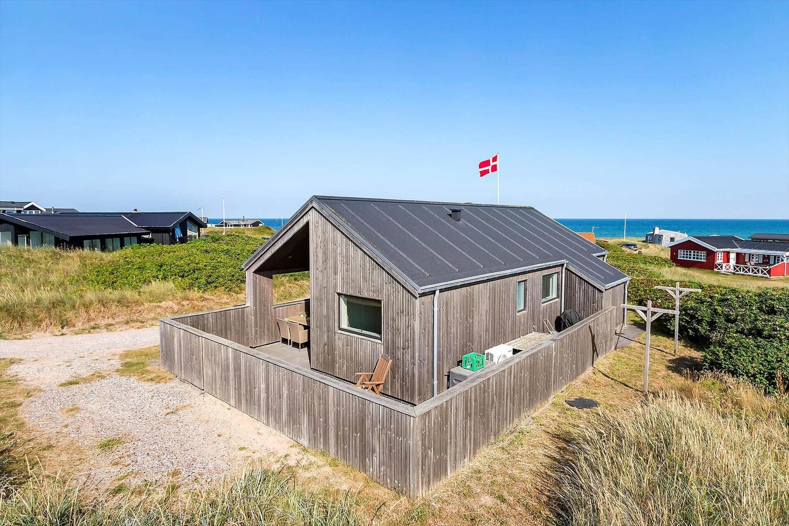 Holzhütte mit Terrasse, daneben Flagge, Strand und Gras