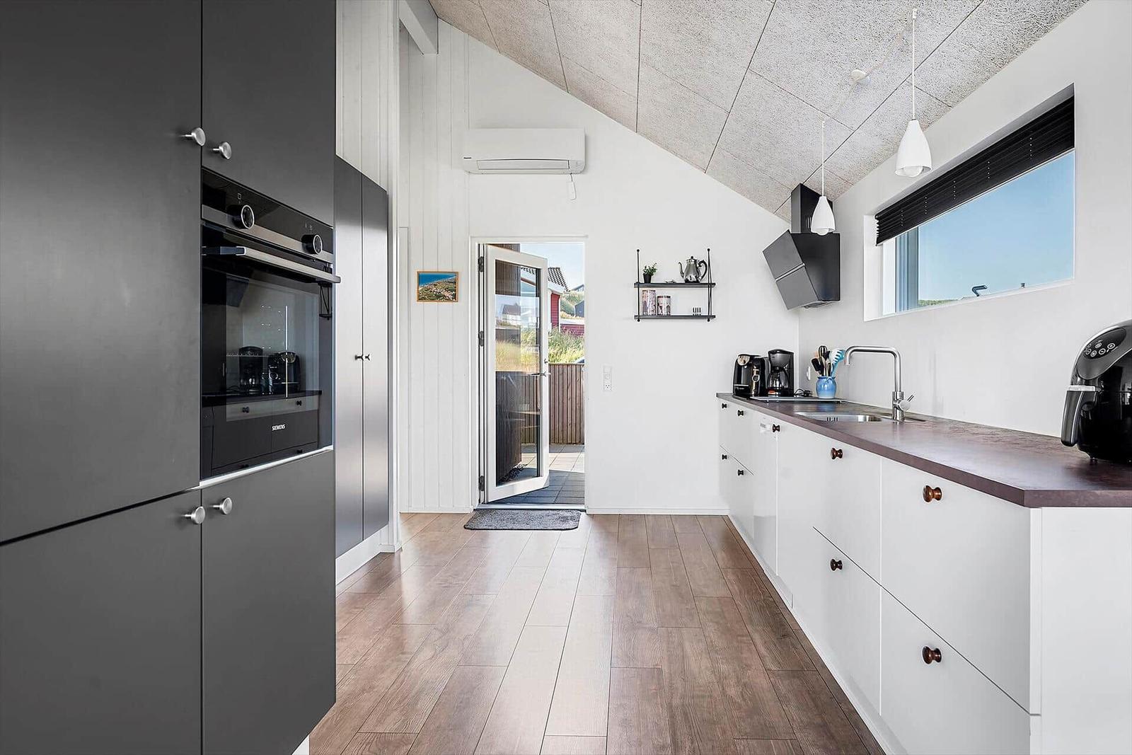Moderne Küche mit dunklen Schränken, Arbeitsplatte und Fenster. Tür führt nach draußen.