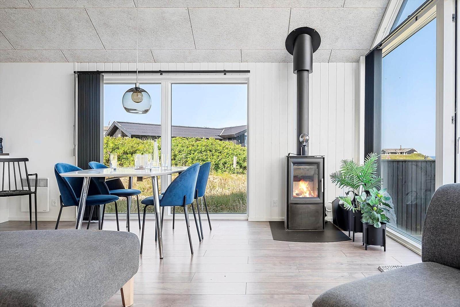 Moderne Wohnküche mit Esstisch, Kamin und großzügigen Fenstern. Blick auf Grünflächen.