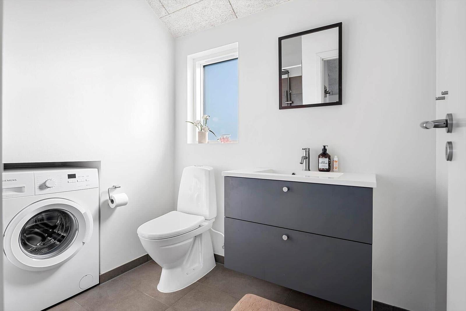 Badezimmer mit Toilette, Waschmaschine und Waschtisch mit Spiegel.