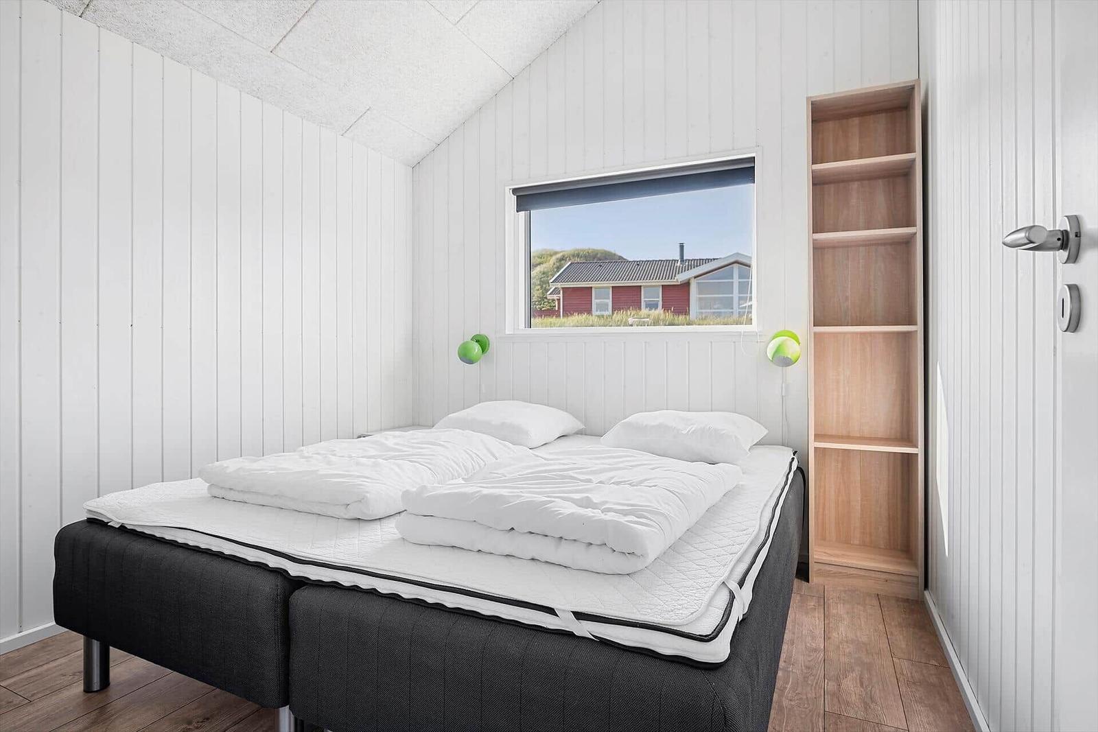 Schlafzimmer mit Bett, Fenster und Holzregal an der Wand.