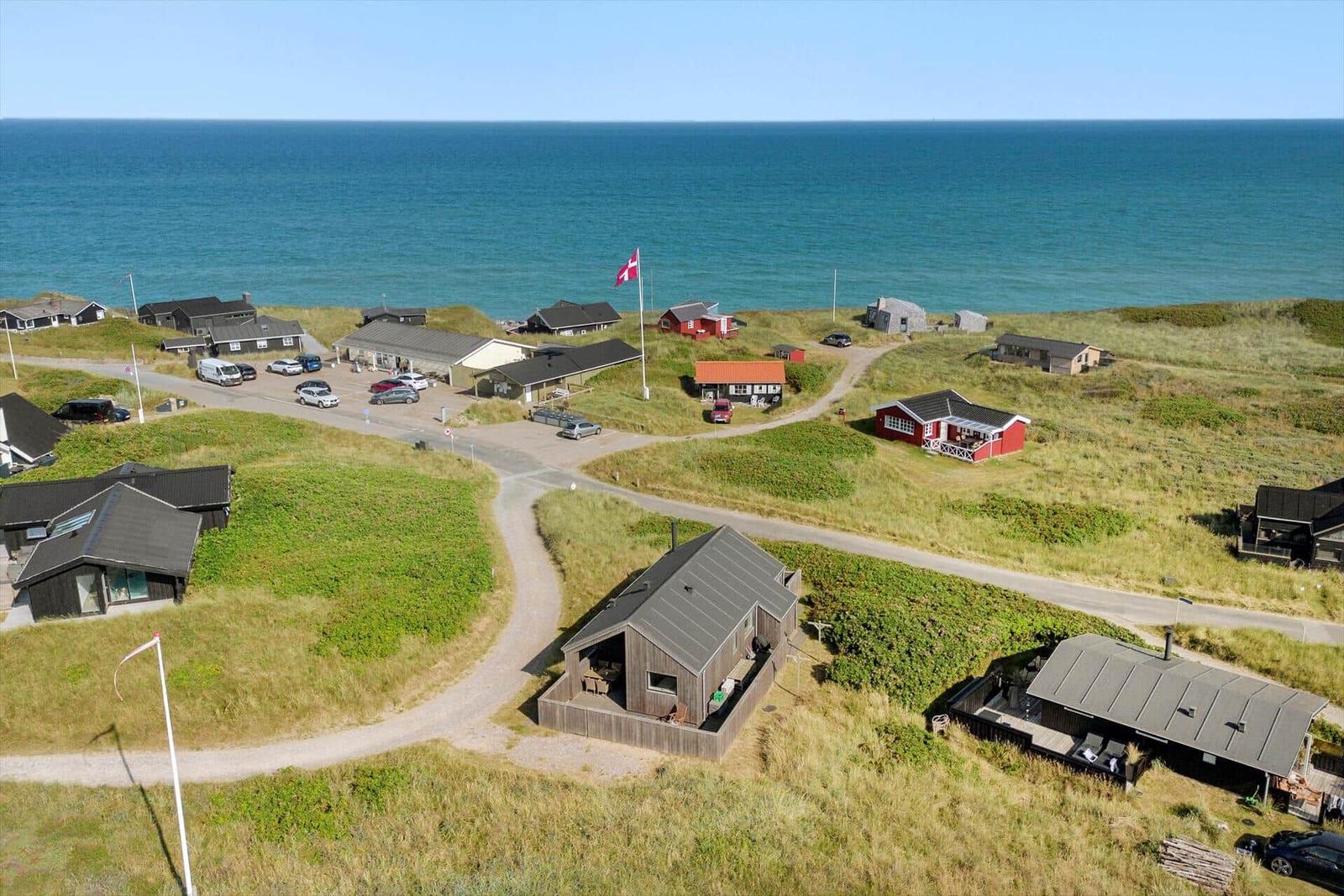 Häuser und Wege auf einer grünen Dünenlandschaft mit Blick auf das Meer.