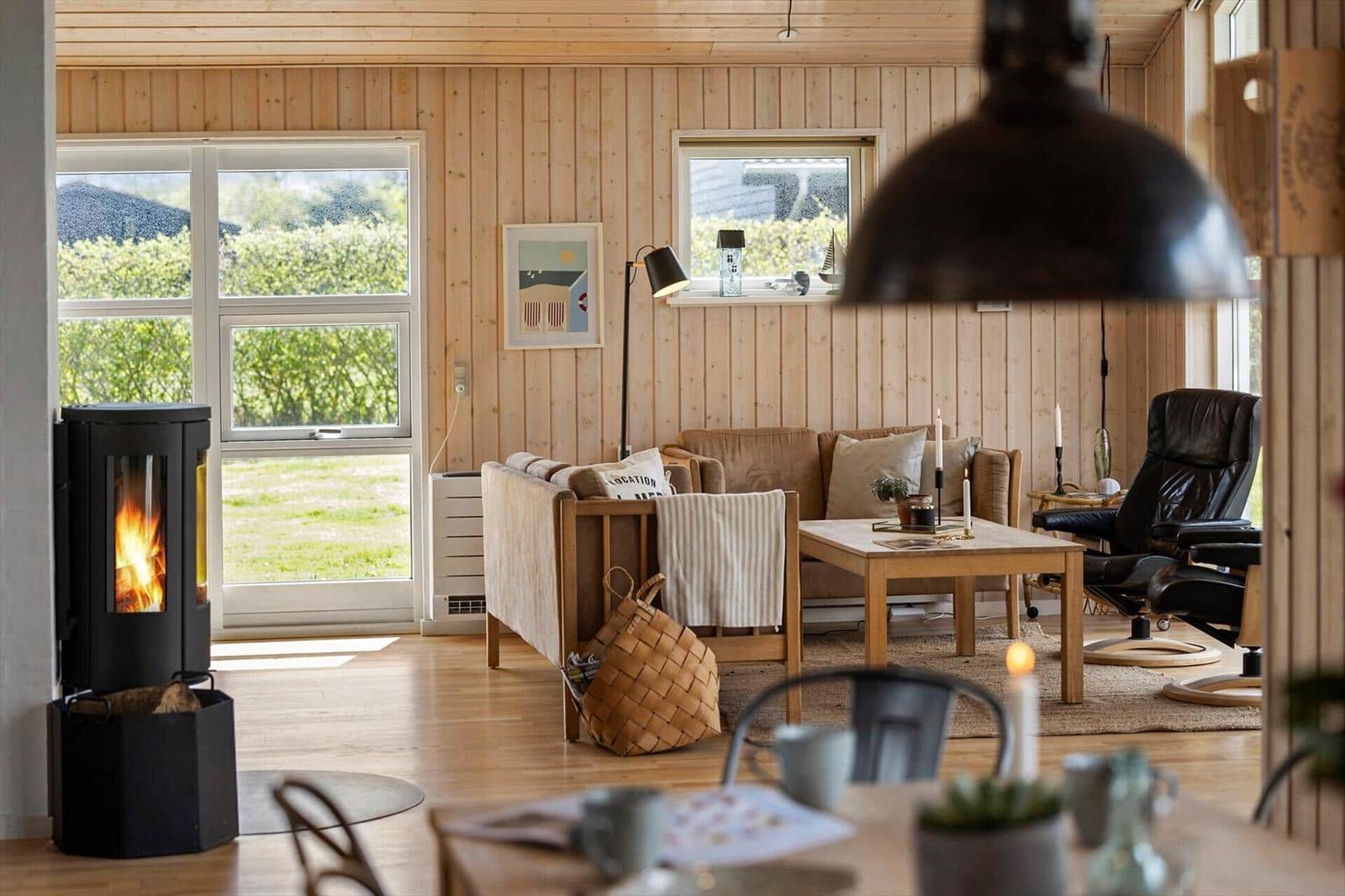Wohnraum mit Holzwand, Sofa, Tisch und Kaminofen. Durchblick auf grünen Garten.